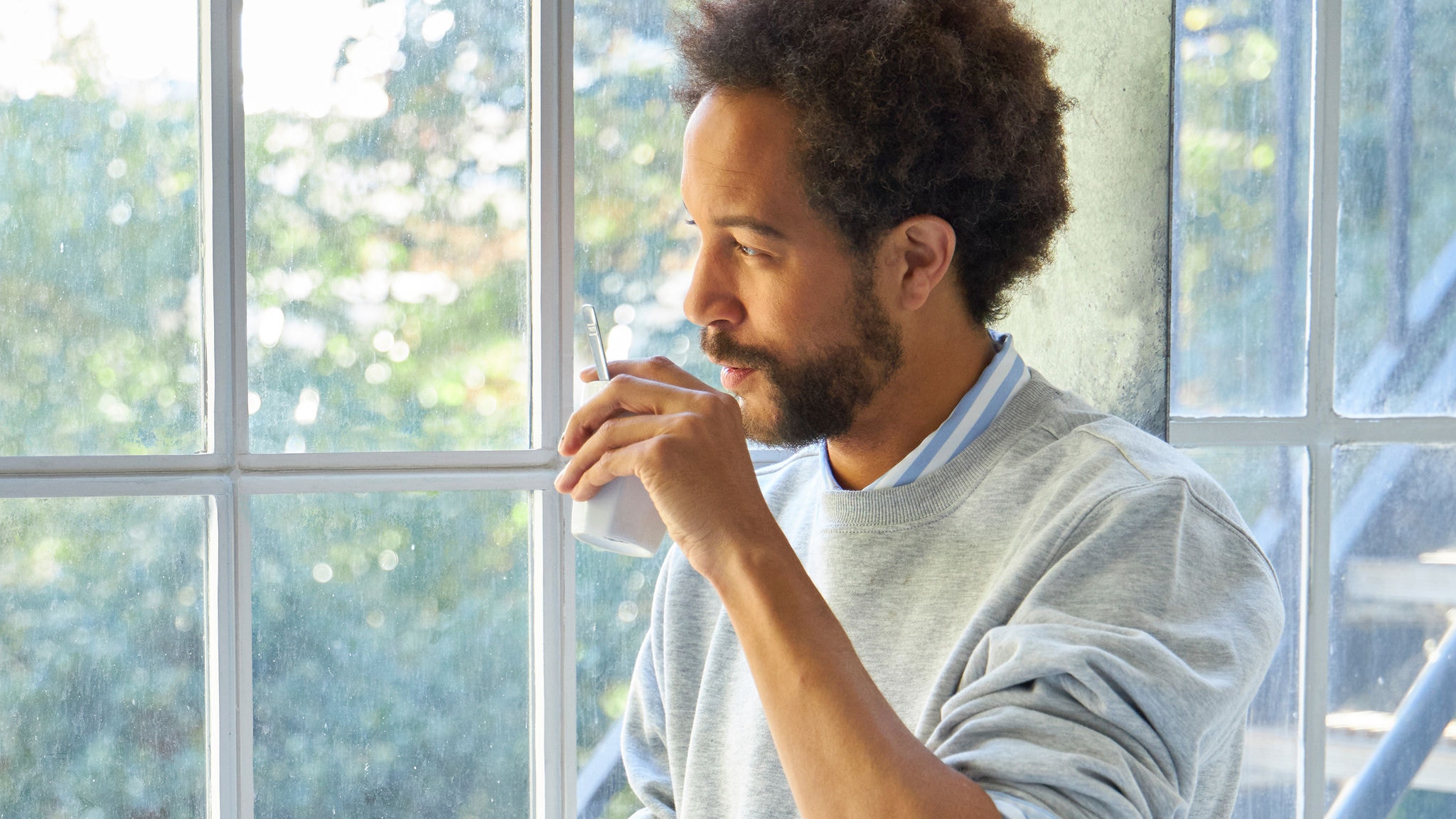 Man drinking from a cup next to big window in sunny weather