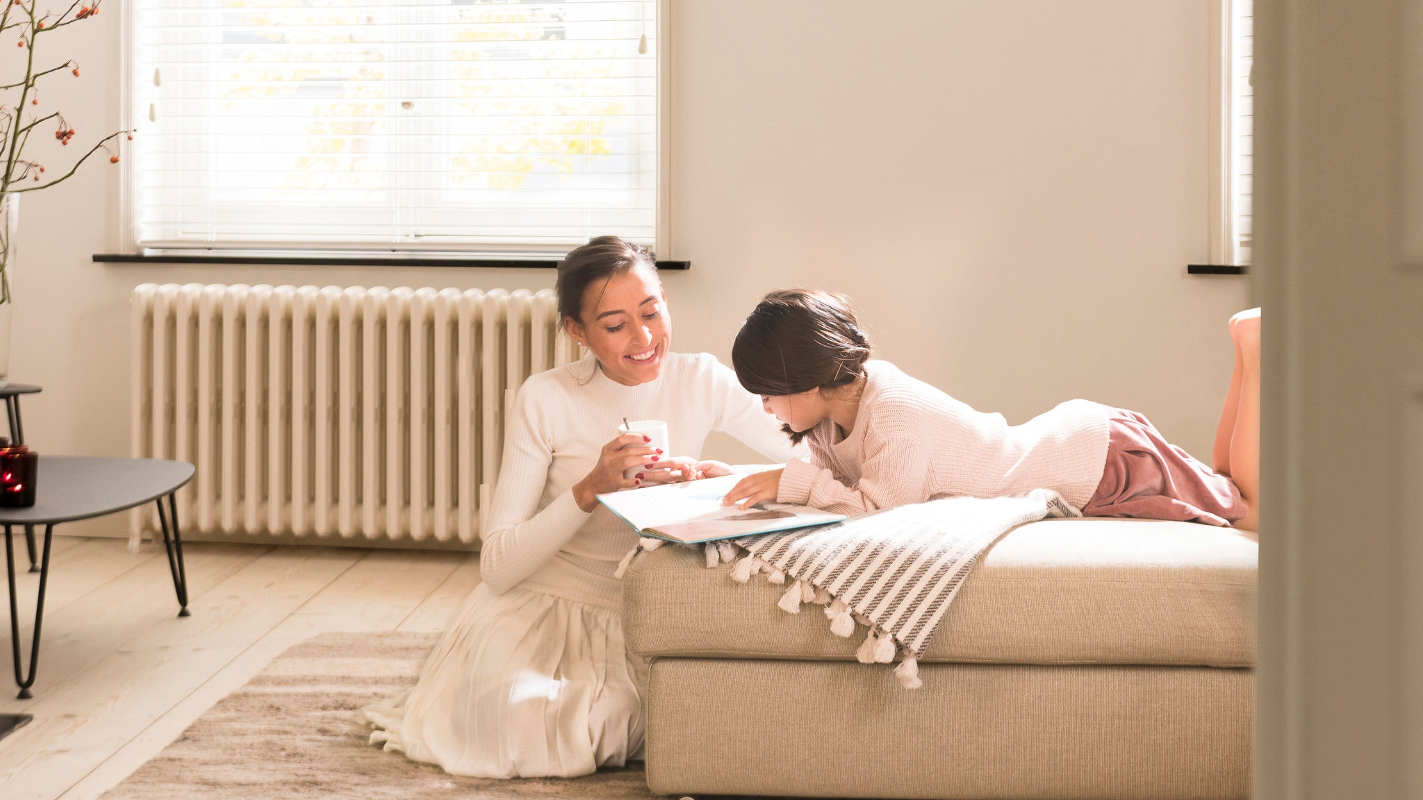 Mother helping daughter to read a book in cosy and warm living room