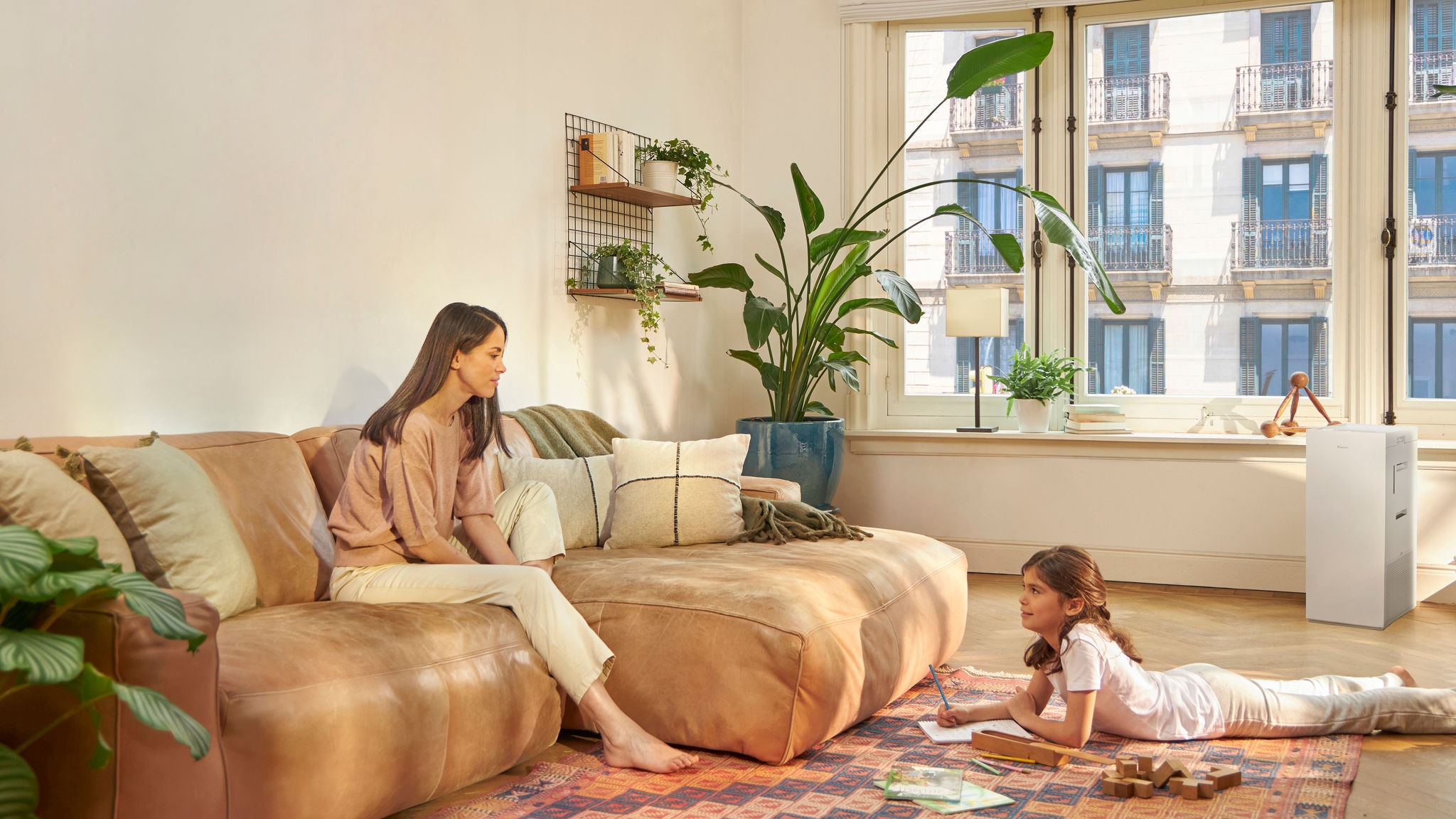 Mother and daughter relaxing and enjoying clean air in the living room, while the daughter is drawing and the mother sitting on the couch