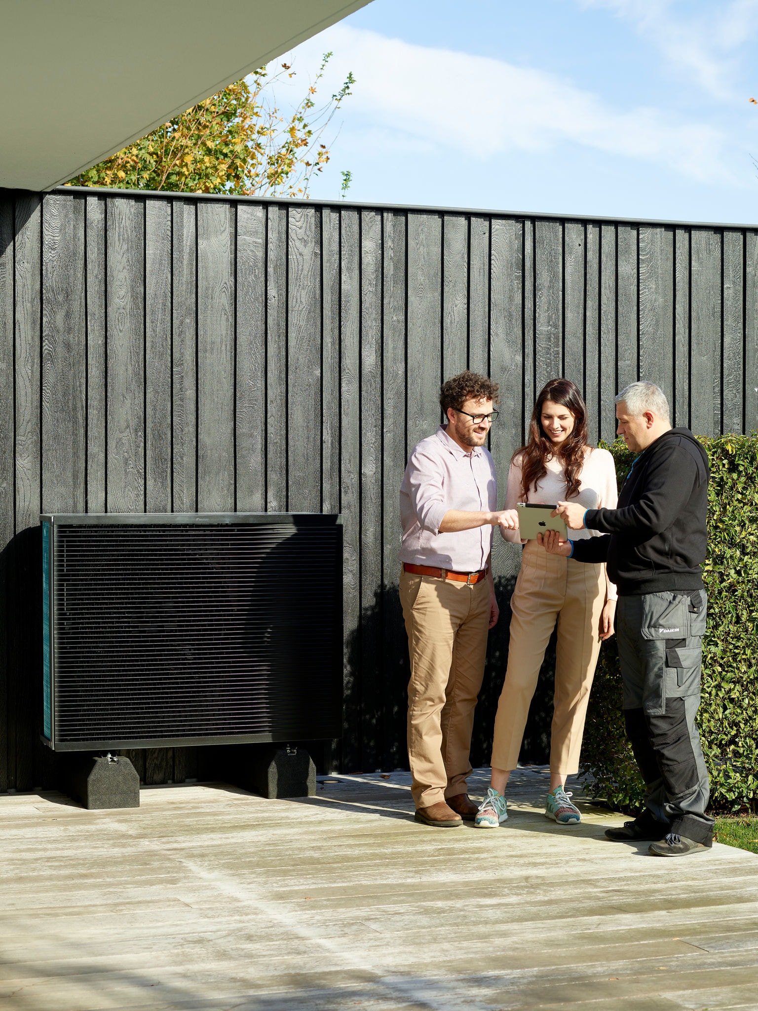 Couple talking to an installer next to the outdoor unit of a Daikin Alterma in their garden