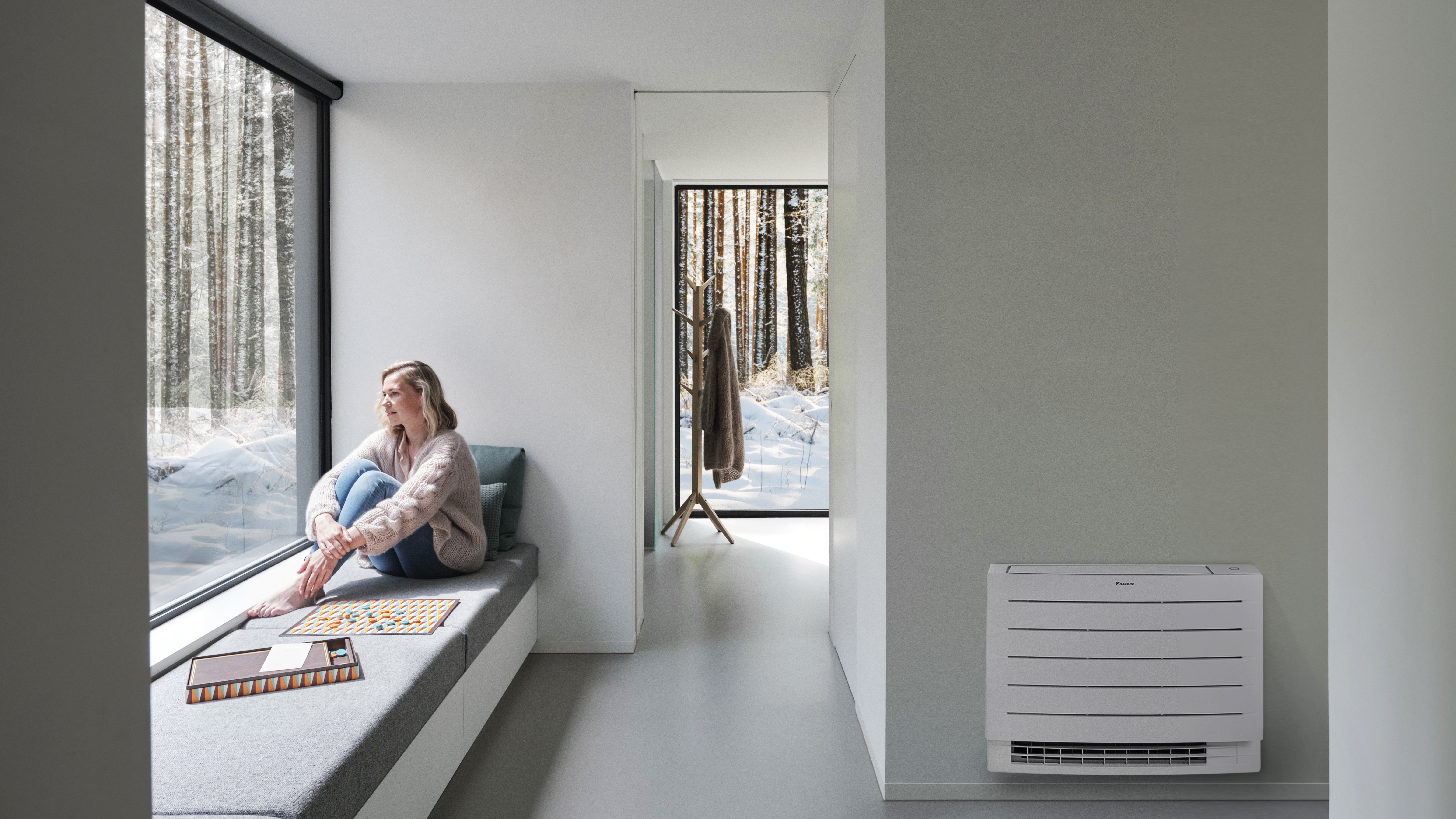 Woman staring at the white snowbed outside her house enjoying a heated home thanks to the Perfera floor-standing unit
